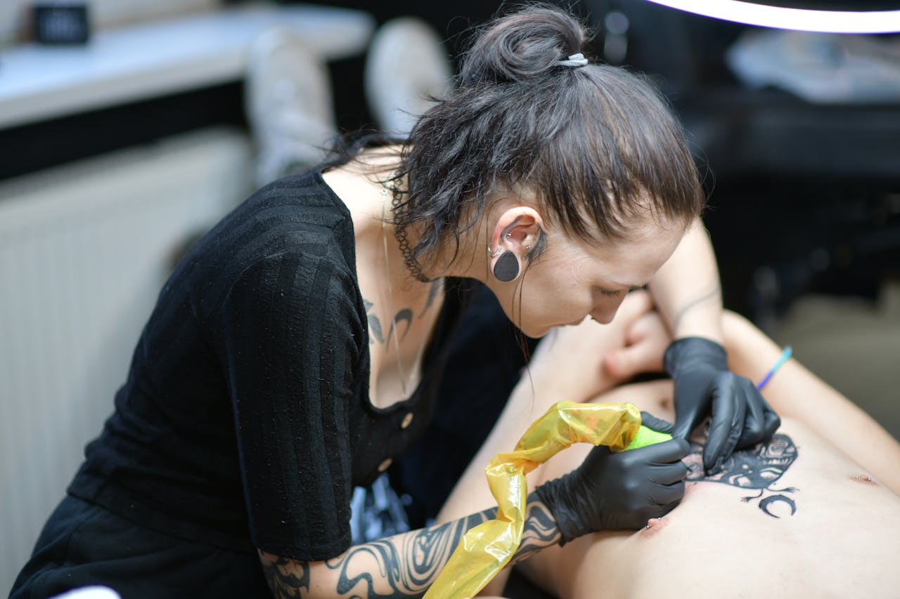 Tattoo artist focuses on creating detailed body art in a studio environment.