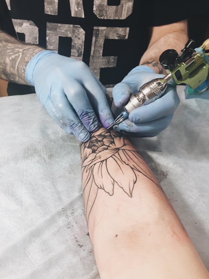 Tattoo artist creating detailed floral design on a client's forearm in studio.